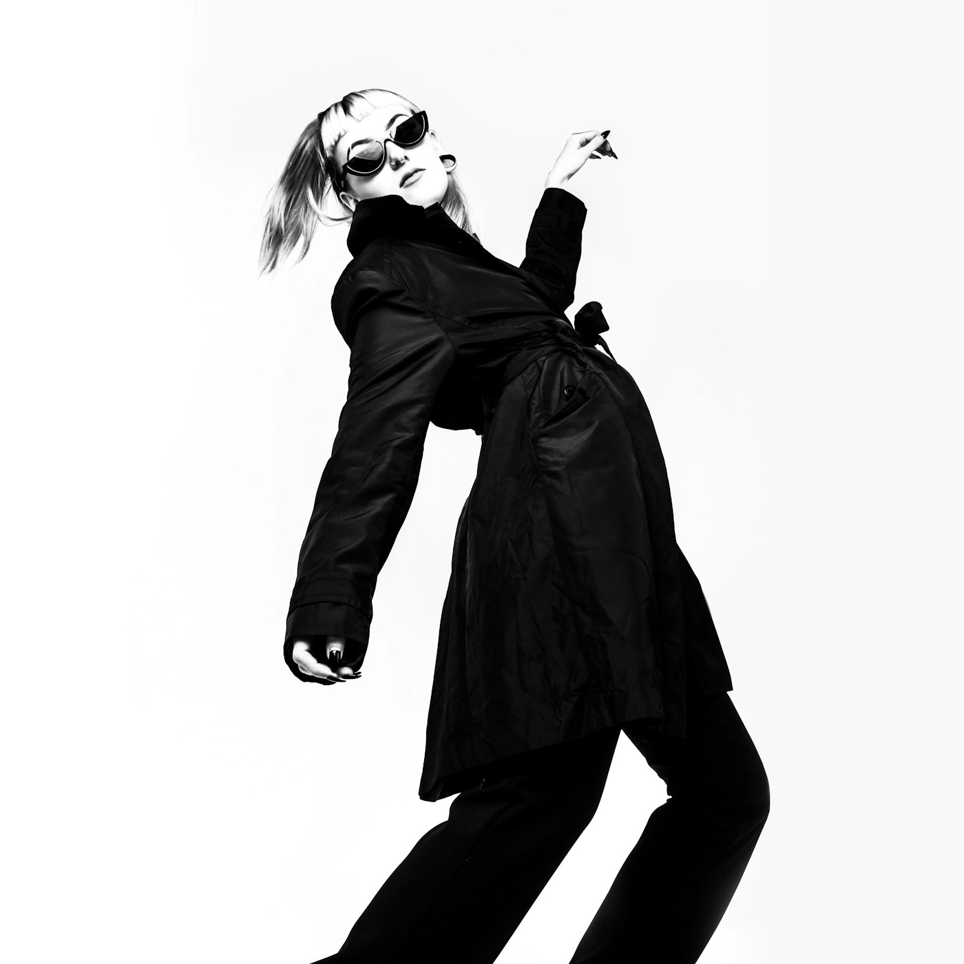 Black-and-white frame of a dancer in a dark coat and sunglasses.